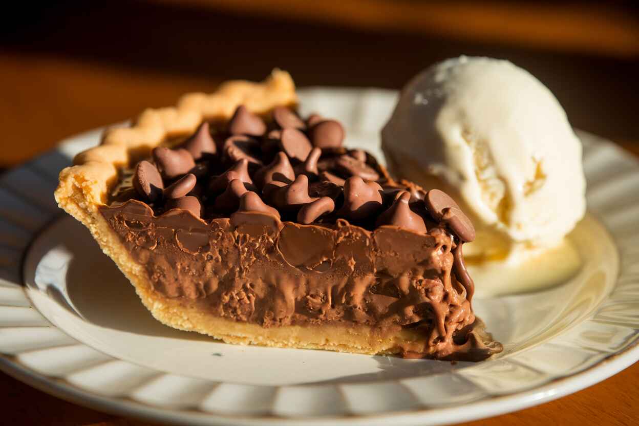 A slice of gooey Toll House pie served with vanilla ice cream on a white plate.