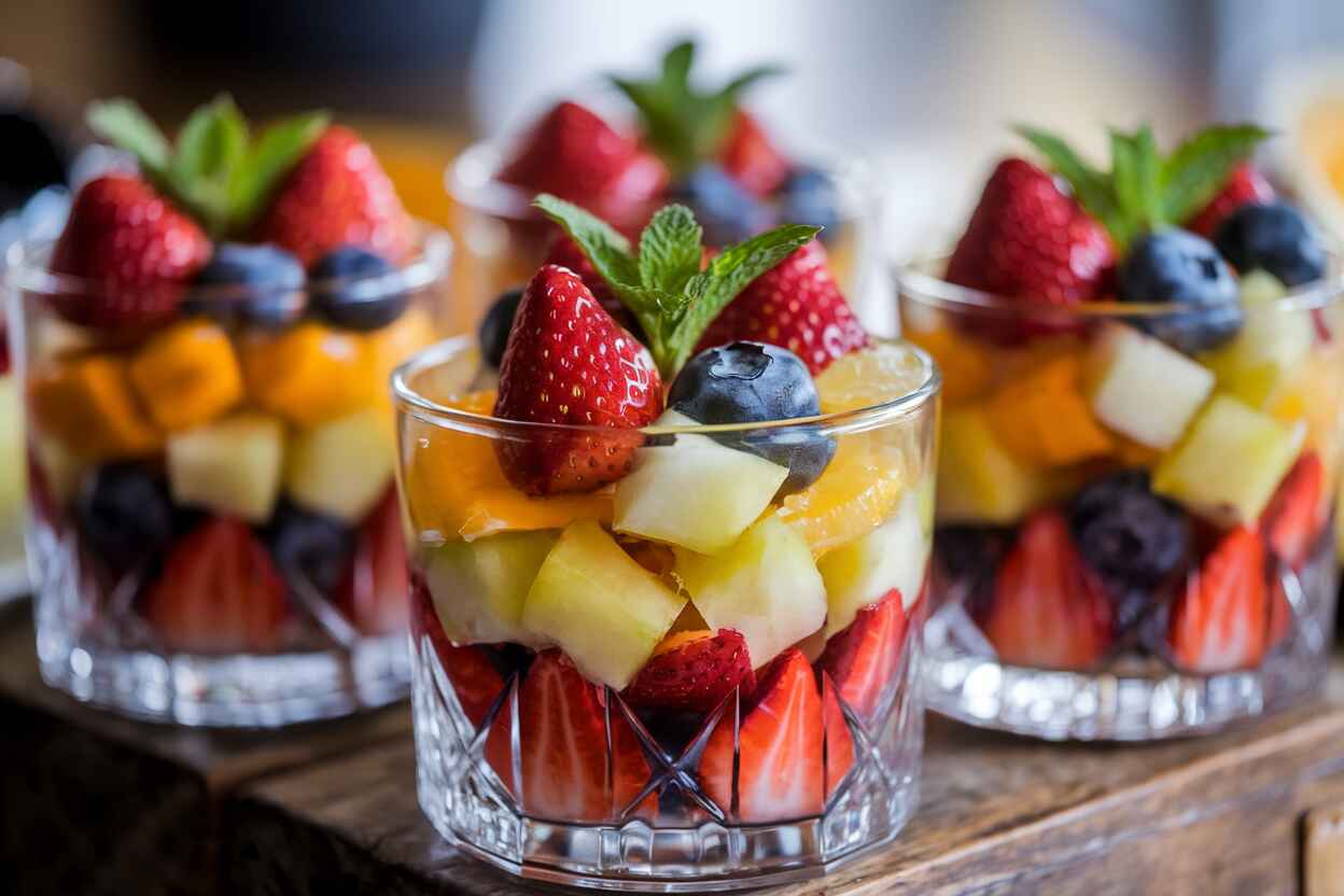 A close-up of colorful fruit cups in clear glass bowls, garnished with mint leaves.