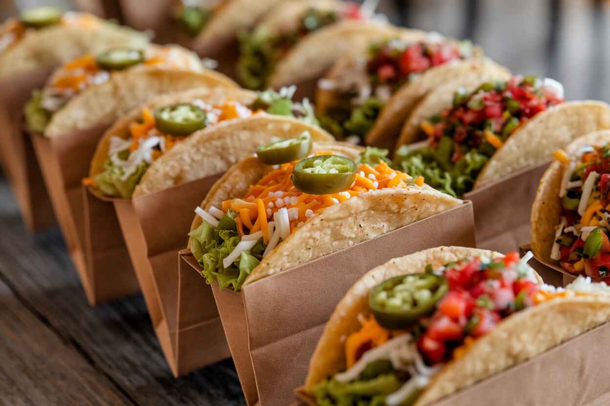 A table with ingredients for walking taco bags, including chips, seasoned meat, cheese, and vegetables.