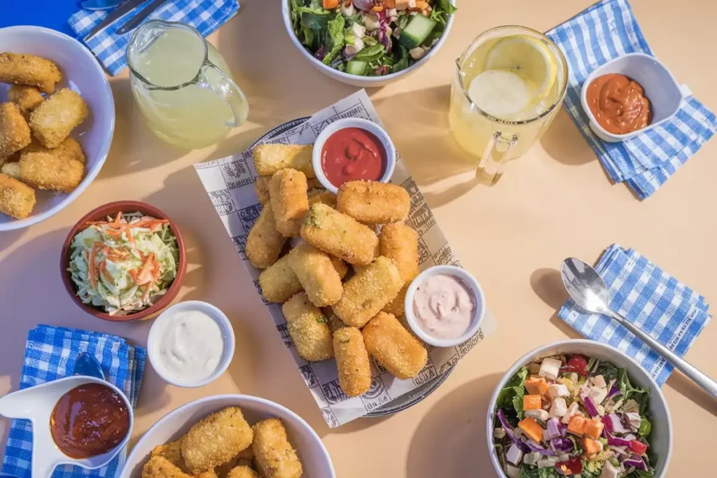 A table spread with corn nuggets, sauces, coleslaw, and salad.