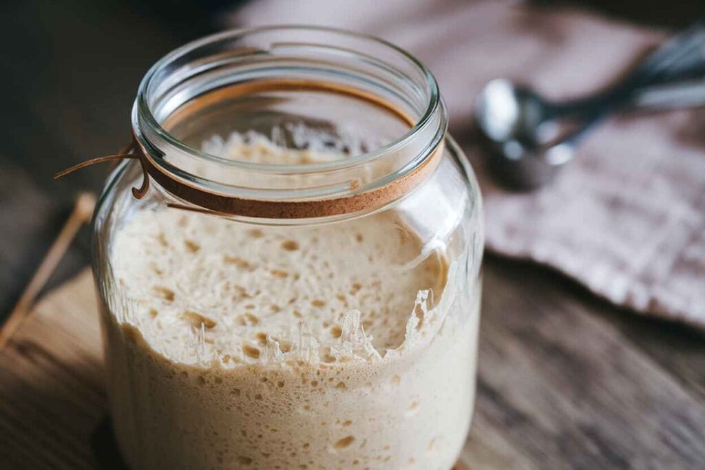 A bubbly gluten-free sourdough bread starter in a glass jar, ready for baking.