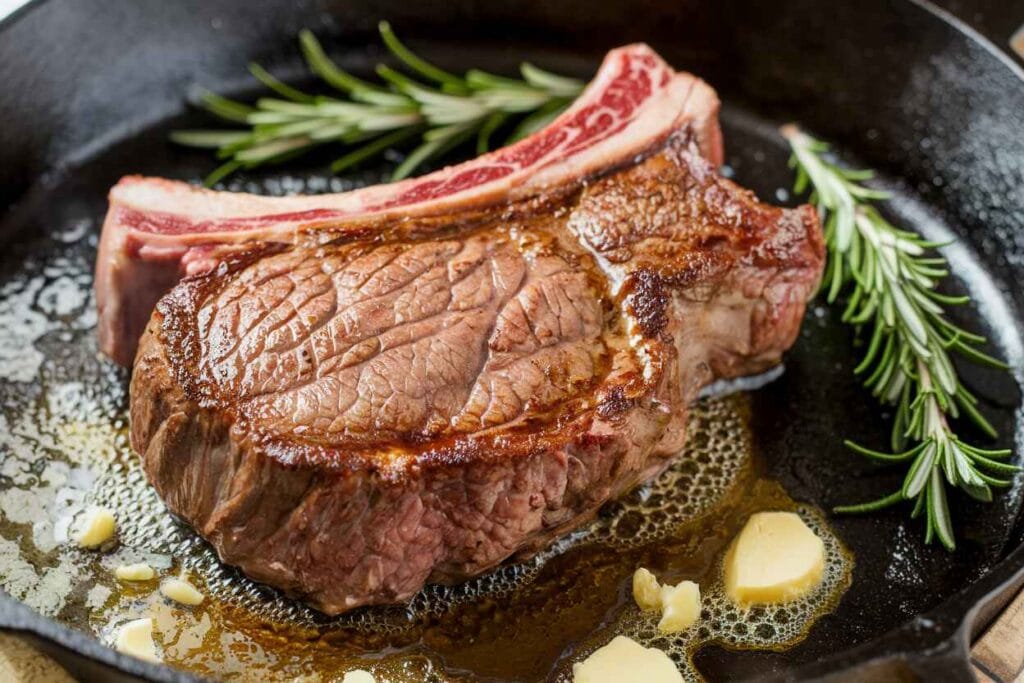 A sizzling ribeye steak searing in a cast-iron pan with butter and garlic.