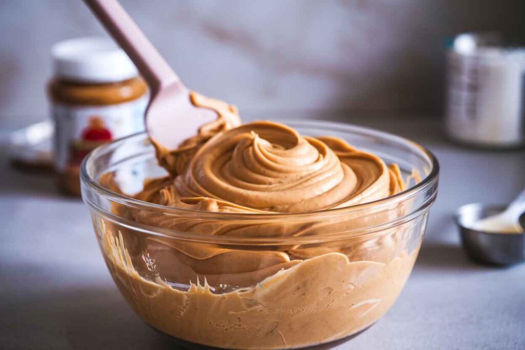 A bowl of creamy peanut butter and frosting mixture being stirred to a smooth, silky consistency.