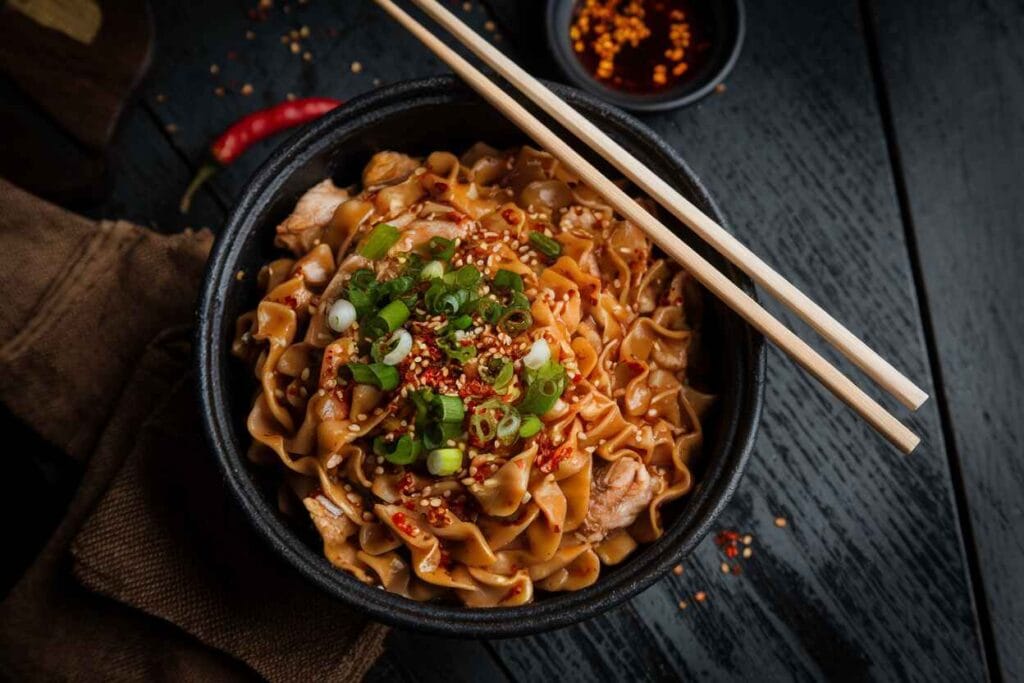 A bowl of Spicy Chicken Mei Fun topped with red chili flakes and fresh herbs.