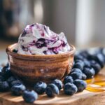 A bowl of homemade blueberry cream cheese with a creamy texture, swirled with fresh blueberry sauce, and surrounded by whole blueberries.